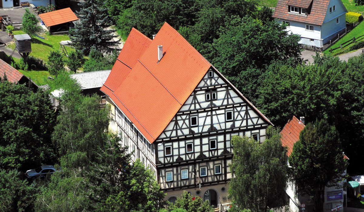 Ein großes Fachwerkhaus mit rotem Dach, umgeben von Bäumen und kleineren Gebäuden. Es wirkt traditionell und ländlich., © Landkreis Göppingen Ein großes Fachwerkhaus mit rotem Dach, umgeben von Bäumen und kleineren Gebäuden. Es wirkt traditionell und ländlich., © Landkreis Göppingen