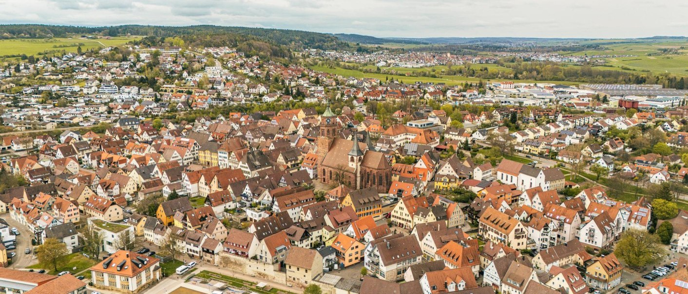 Luftaufnahme von Weil der Stadt mit einer zentralen Kirche und umliegenden Häusern. Die Landschaft ist von grünen Hügeln umgeben., © Stuttgart-Marketing GmbH, Sarah Schmid Luftaufnahme von Weil der Stadt mit einer zentralen Kirche und umliegenden Häusern. Die Landschaft ist von grünen Hügeln umgeben., © Stuttgart-Marketing GmbH, Sarah Schmid
