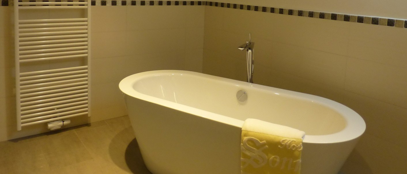 Freistehende Badewanne in einem modernen Badezimmer mit Handtuch und Heizkörper an der Wand., © Hotel & Restaurant Sonne