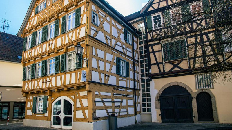 Fachwerkgeb&auml;ude in Schorndorf mit gr&uuml;nen Fensterl&auml;den. Ein Baum steht im Vordergrund, daneben ein modernes Geb&auml;ude., &copy; Stuttgart-Marketing GmbH, Sarah Schmid