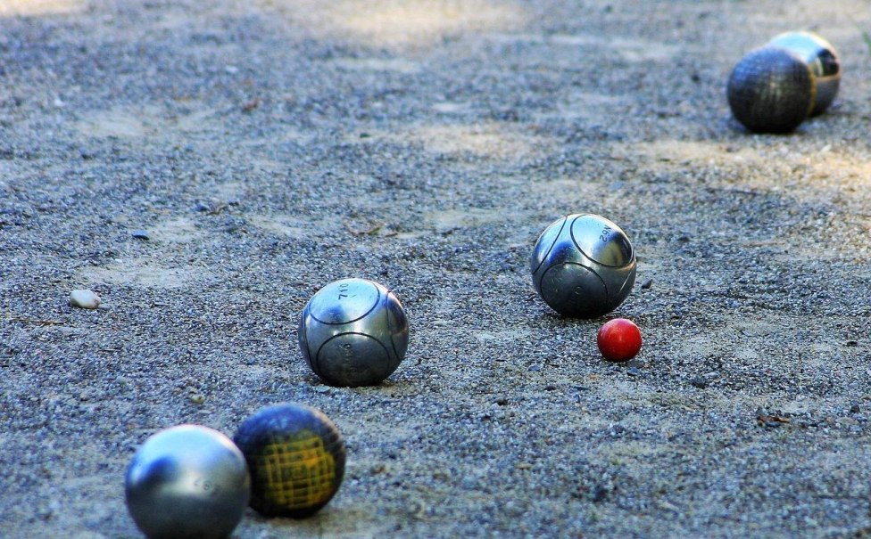 Metallene Boule-Kugeln liegen auf einem Sandplatz um eine kleine rote Zielkugel verteilt. Das Bild zeigt eine typische Spielsituation beim Boule., &copy; boule-3058654_1280_JuergenSieber_Pixabay