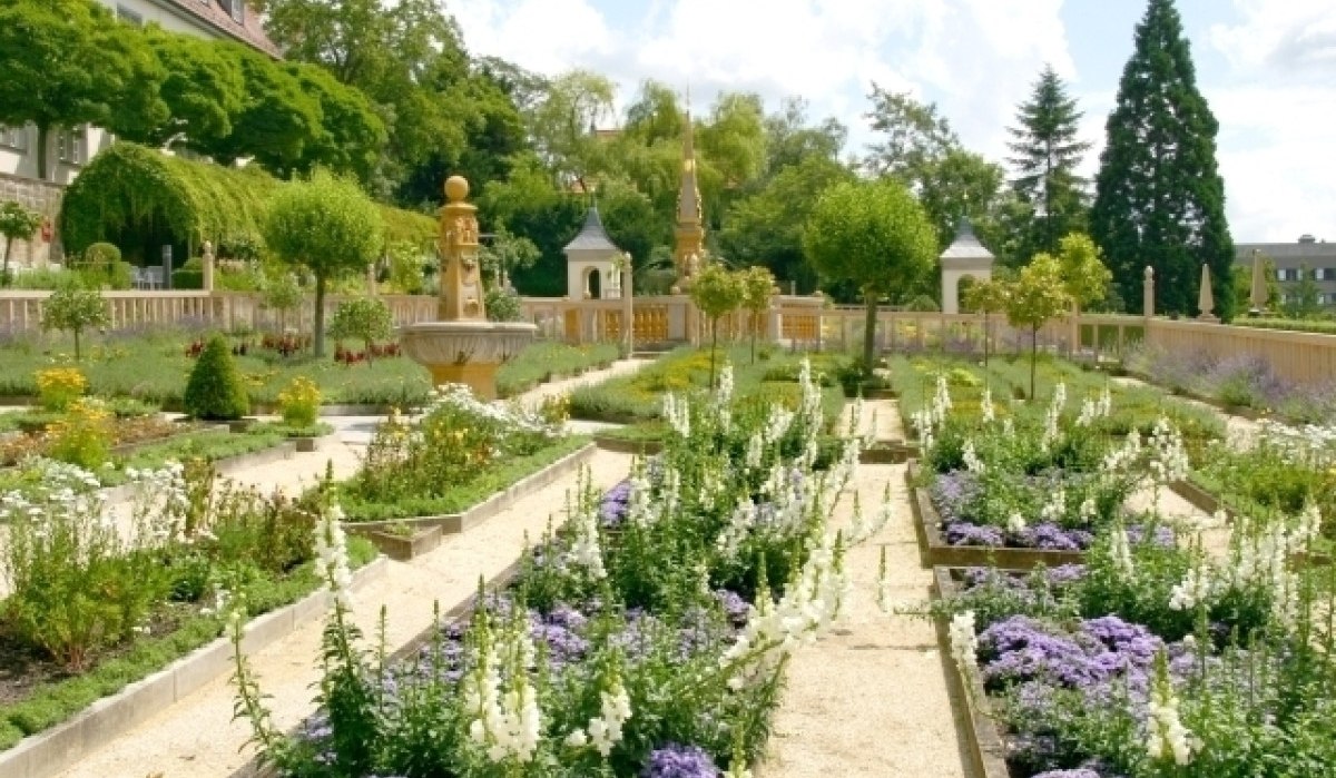 Ein gepflegter Garten mit Blumenbeeten, Bäumen und einem Brunnen im Pomeranzengarten, Leonberg, bei sonnigem Wetter., © Stadt Leonberg