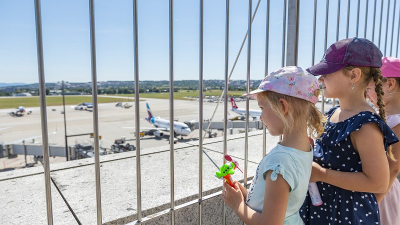 Kinder stehen auf der Besucherterrasse des Stuttgarter Flughafens und schauen durch ein Gitter auf das Rollfeld mit Flugzeugen., &copy; Flughafen Stuttgart