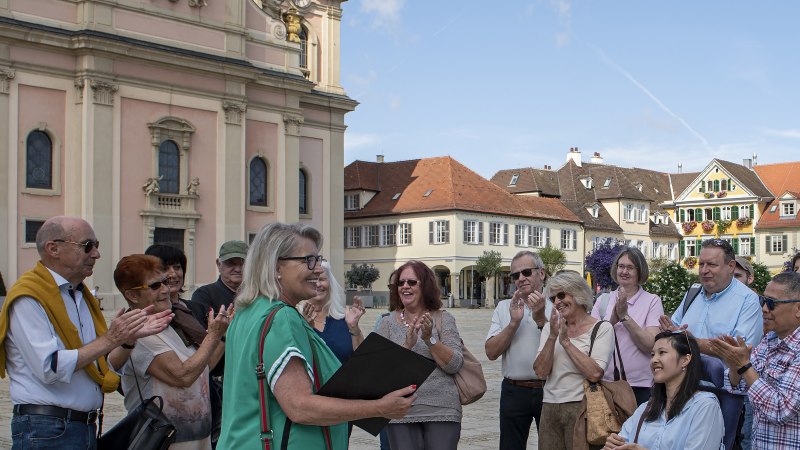 Gruppe applaudiert einer Frau vor einem historischen Gebäude in Ludwigsburg. Sonniger Tag, fröhliche Stimmung., © Tourismus & Events Ludwigsburg, Yakup Zeyrek