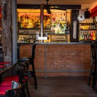 Gemütliche Bar mit Backsteinwand, gut bestücktem Regal und roten Sitzpolstern. Schwarze Tische und Stühle, warme Beleuchtung., © Café Bar Zill
