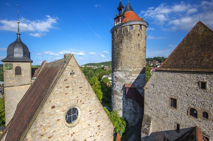 Historische Gebäude in Besigheim mit einem markanten Turm und alten Steinhäusern. Der blaue Himmel und die grüne Landschaft ergänzen die mittelalterliche Szenerie., © Stadt Besigheim