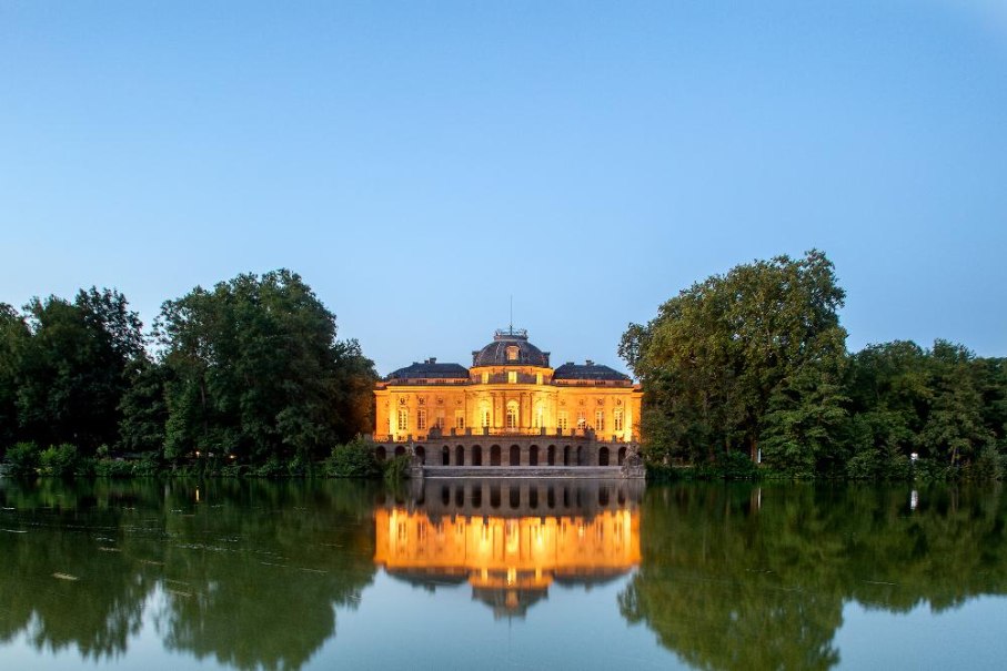 Das Seeschloss Monrepos erstrahlt in warmem Licht, umgeben von B&auml;umen und spiegelt sich im ruhigen Wasser wider. Der Himmel ist klar und blau., &copy; Seeschloss Monrepos &copy; Daniel Stauch