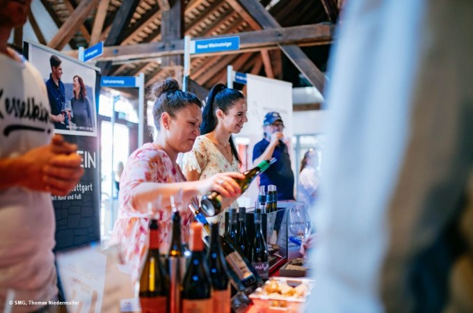 Zwei Frauen schenken Wein bei einer Veranstaltung ein. Im Hintergrund sind Werbebanner und Weinflaschen zu sehen., © Stuttgart-Marketing GmbH, Thomas Niedermüller