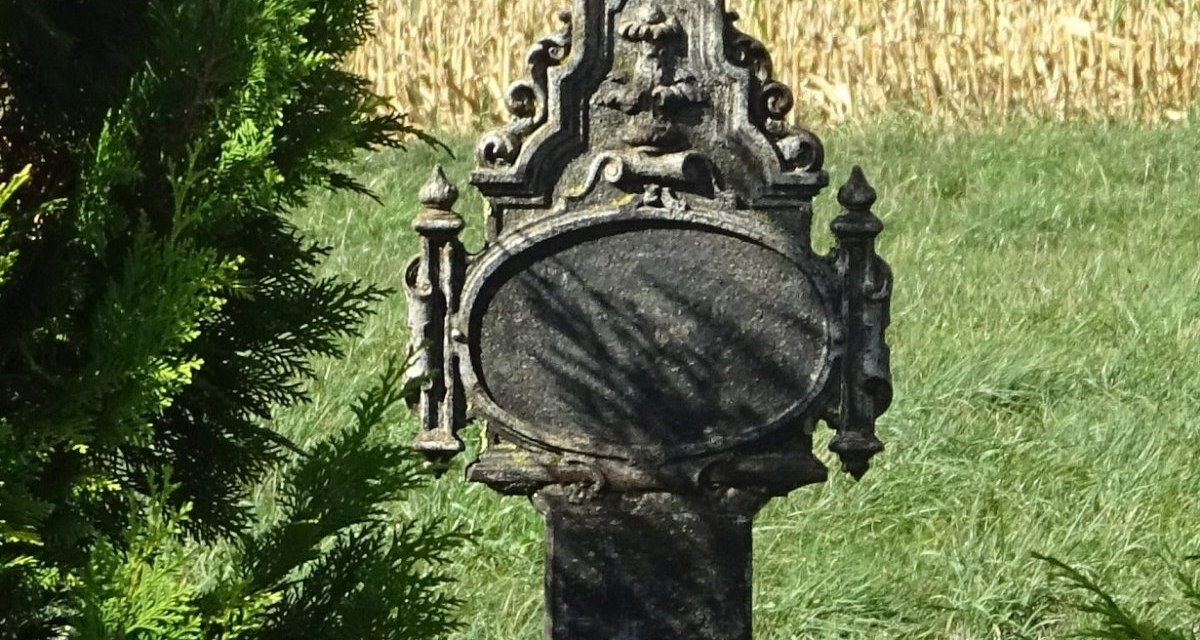 Ein verziertes Steinkreuz mit Jesusfigur steht in einer gr&uuml;nen Landschaft, umgeben von B&uuml;schen und Feldern., &copy; Foto: Cornelia Steinbach