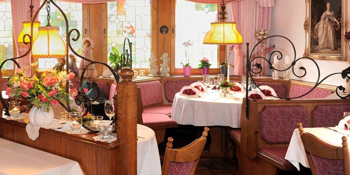 Ein gemütliches Restaurant mit Holzmöbeln, Blumenarrangements und dekorativen Lampen. Die Tische sind elegant gedeckt, und es gibt bunte Fensterdekorationen., © Hotel Lamm Hegnach