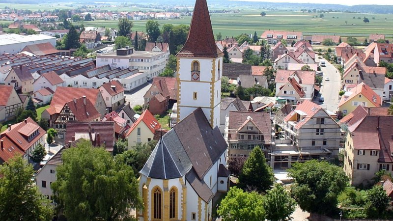Luftaufnahme von Holzgerlingen mit einer Kirche im Vordergrund, umgeben von H&auml;usern und gr&uuml;ner Landschaft im Hintergrund., &copy; Natur.Nah. Sch&ouml;nbuch & Heckeng&auml;u