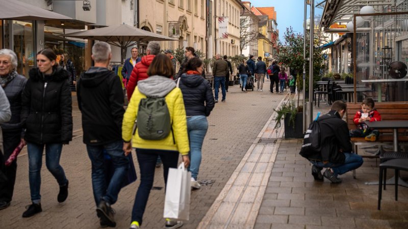 Belebte Einkaufsstra&szlig;e mit Menschen, die spazieren gehen. Gesch&auml;fte und Caf&eacute;s s&auml;umen den Weg. Ein Kind sitzt mit einem Erwachsenen auf einer Bank., &copy; Ludwigsburger Innenstadt e.V. (LUIS)