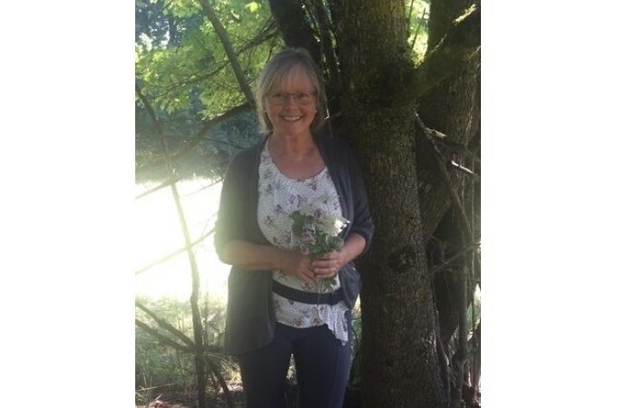 Eine Frau steht lächelnd neben einem Baum und hält einen Strauß Wildkräuter. Sonnenlicht fällt durch die Blätter und erzeugt ein angenehmes Lichtspiel., © Touristik und Marketing GmbH Eine Frau steht lächelnd neben einem Baum und hält einen Strauß Wildkräuter. Sonnenlicht fällt durch die Blätter und erzeugt ein angenehmes Lichtspiel., © Touristik und Marketing GmbH