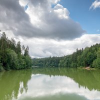 Der Herrenbachstausee in Schorndorf, umgeben von dichten W&auml;ldern und reflektiert im ruhigen Wasser. Wolken ziehen &uuml;ber den blauen Himmel.