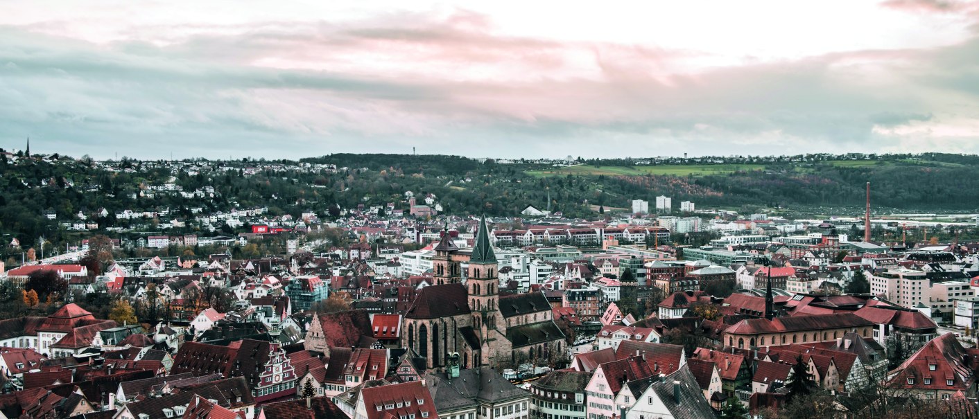 Panoramablick auf Esslingen von der Burg aus, mit roten Dächern, einer Kirche und grünen Hügeln im Hintergrund unter bewölktem Himmel., © Esslingen Markt und Event GmbH (EME)