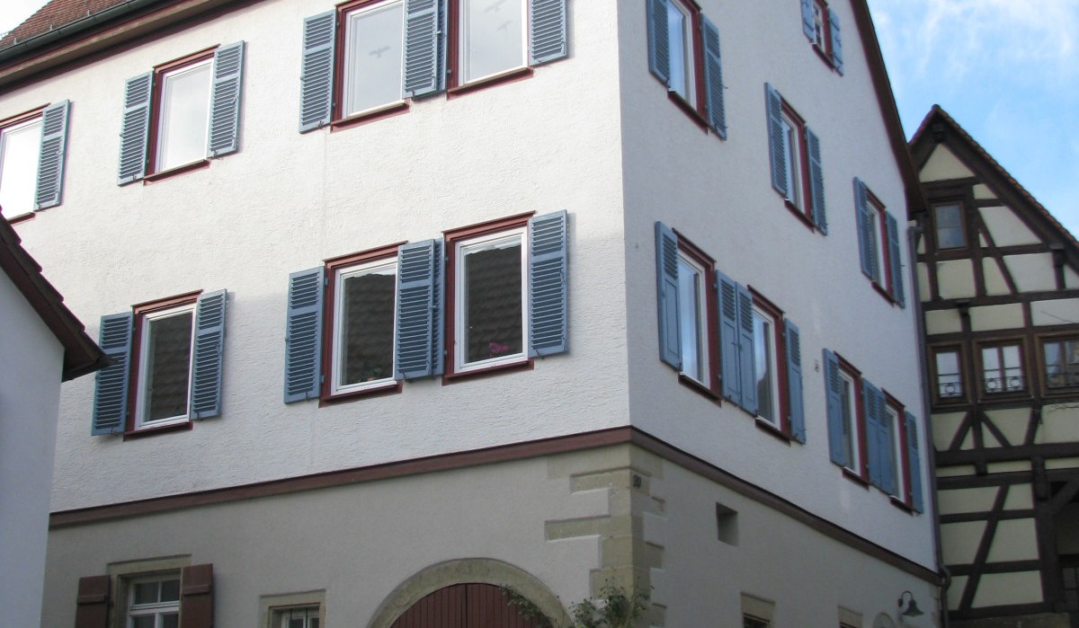 Ein dreistöckiges, weißes Gebäude mit roten Dachziegeln und blauen Fensterläden. Es hat einen großen Torbogen und steht auf einem gepflasterten Platz., © Land der 1000 Hügel - Kraichgau-Stromberg