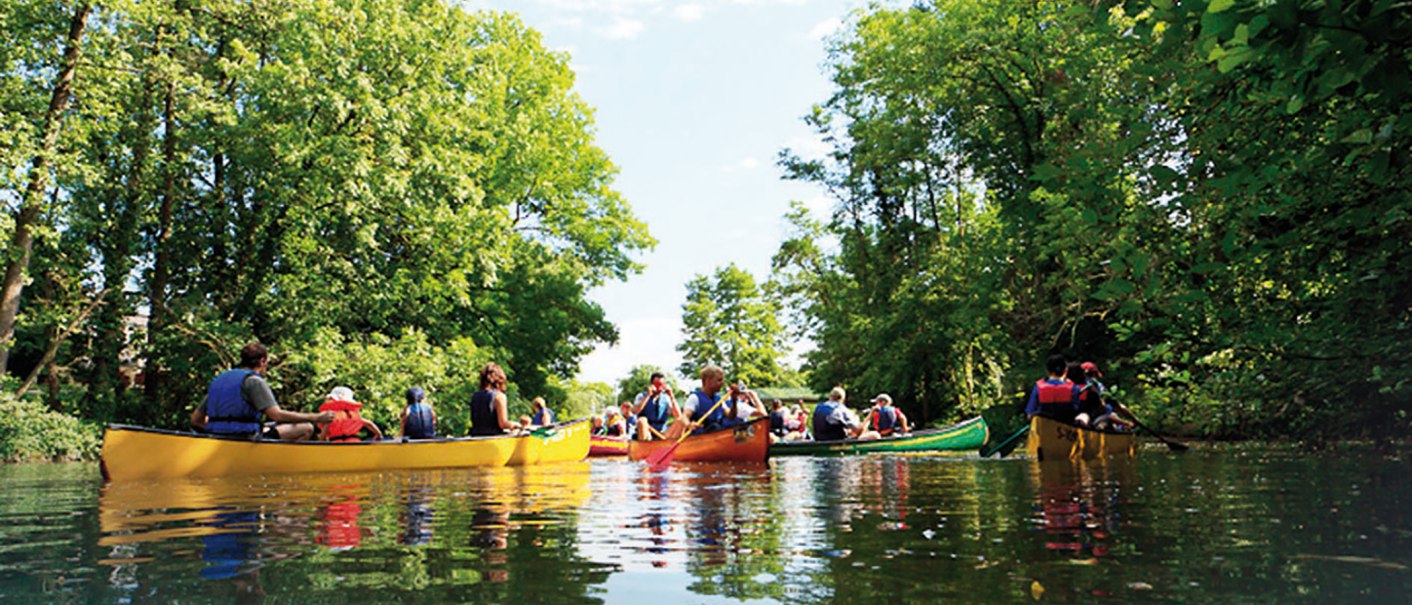 Gruppe von Menschen paddelt in bunten Kanus auf einem ruhigen Fluss, umgeben von üppigem Grün und Bäumen., © WTM GmbH Waiblingen