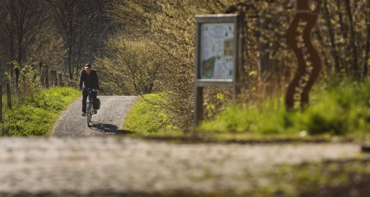Person auf Fahrrad auf ländlichem Weg, umgeben von Bäumen und einem Schild., © Natur.Nah. Schönbuch & Heckengäu Person auf Fahrrad auf ländlichem Weg, umgeben von Bäumen und einem Schild., © Natur.Nah. Schönbuch & Heckengäu