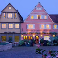 Ein malerisches Dorf bei Dämmerung mit einem historischen Gasthaus und einer Metzgerei. Blumen und ein Brunnen schmücken den Platz. Ein malerisches Dorf bei Dämmerung mit einem historischen Gasthaus und einer Metzgerei. Blumen und ein Brunnen schmücken den Platz.