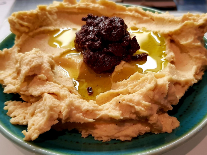 Cremiger Hummus auf einem Teller, garniert mit Olivenöl und einer dunklen Paste in der Mitte., © Kultweine-Kochwelten-Kunstücke - Kochschule Sonja Lenz Cremiger Hummus auf einem Teller, garniert mit Olivenöl und einer dunklen Paste in der Mitte., © Kultweine-Kochwelten-Kunstücke - Kochschule Sonja Lenz