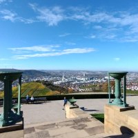 Panoramablick vom Rotenberg auf Stuttgart, umgeben von Weinbergen. Zwei dekorative Säulen im Vordergrund, blauer Himmel und vereinzelte Wolken.