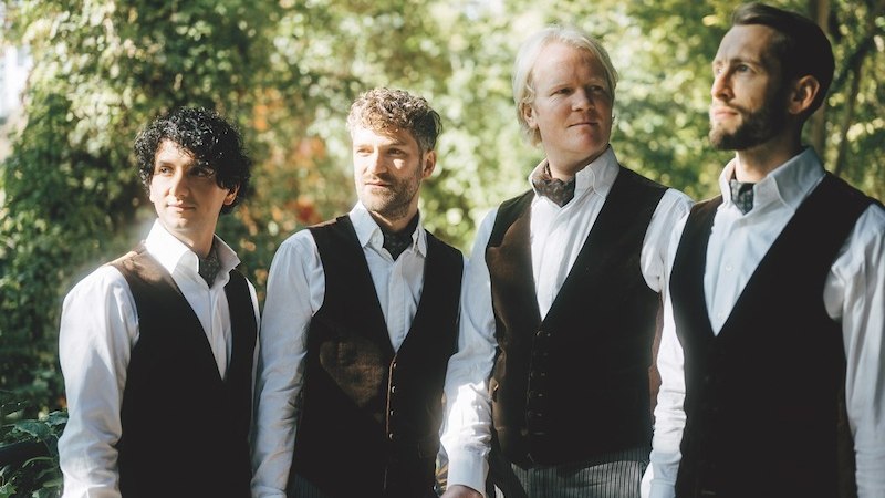 Vier M&auml;nner in eleganter Kleidung stehen im Freien und blicken in verschiedene Richtungen. Sie tragen Westen und Hemden, umgeben von gr&uuml;ner Natur., &copy; Kulturstiftung Hohenlohe