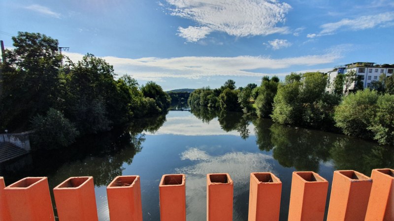 Blick von der Ottosteg-Brücke in Plochingen auf einen ruhigen Fluss, umgeben von Bäumen und Gebäuden, unter einem klaren blauen Himmel., © Kulturamt Plochingen