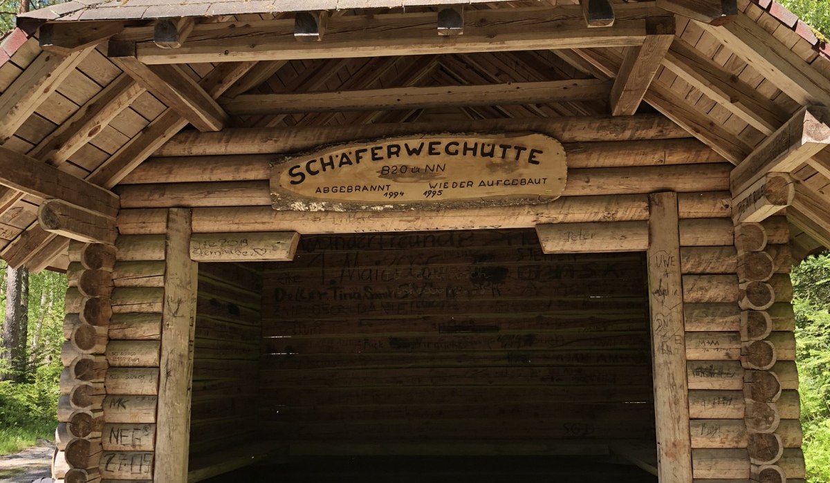 Eine rustikale Holzhütte im Wald, genannt 'Schäferweghütte', mit einem Schild über dem Eingang. Umgeben von hohen Bäumen., © Nördlicher Schwarzwald Eine rustikale Holzhütte im Wald, genannt 'Schäferweghütte', mit einem Schild über dem Eingang. Umgeben von hohen Bäumen., © Nördlicher Schwarzwald