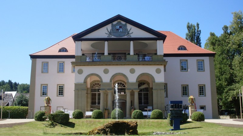 Schloss Dätzingen mit symmetrischer Fassade, rotem Dach und einem Brunnen im Vordergrund. Der Himmel ist klar und blau., © Natur.Nah. Schönbuch & Heckengäu Schloss Dätzingen mit symmetrischer Fassade, rotem Dach und einem Brunnen im Vordergrund. Der Himmel ist klar und blau., © Natur.Nah. Schönbuch & Heckengäu