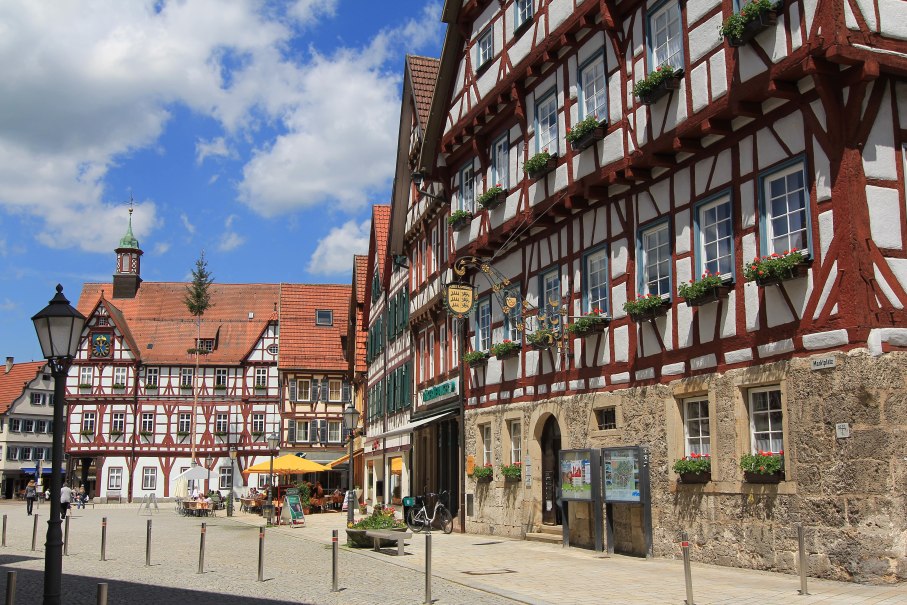 Fachwerkhäuser am Marktplatz von Bad Urach, blauer Himmel mit Wolken, Menschen sitzen draußen, Blumen schmücken die Fenster., © Armin Dieter