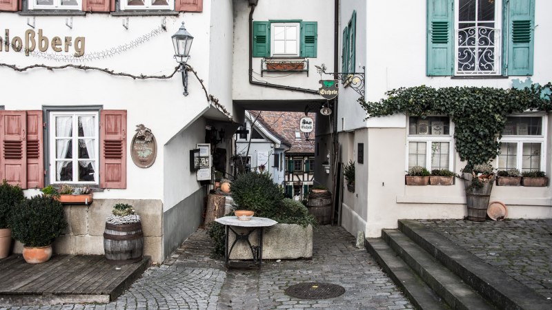 Schmale Gasse in einer Altstadt mit Fachwerkhäusern, Pflanzen in Töpfen und dekorativen Schildern. Kopfsteinpflaster und Treppenstufen., © Martina Naumov Schmale Gasse in einer Altstadt mit Fachwerkhäusern, Pflanzen in Töpfen und dekorativen Schildern. Kopfsteinpflaster und Treppenstufen., © Martina Naumov