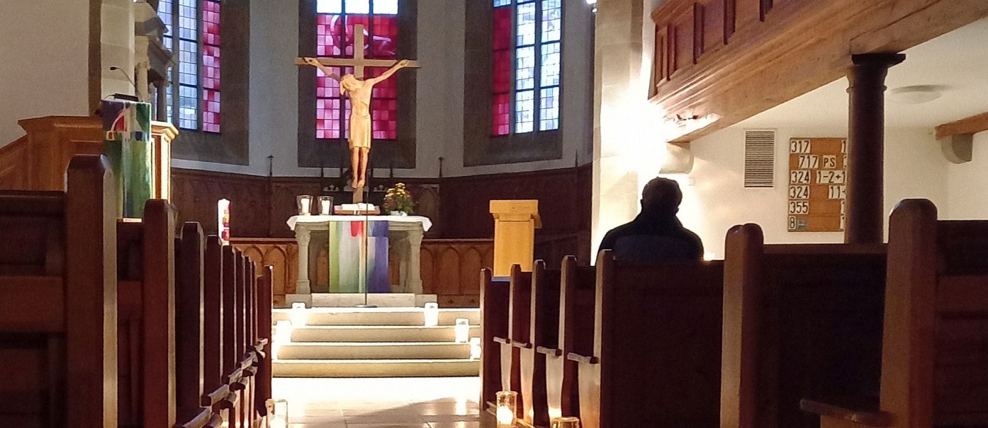 Blick in den Chor der Stadtkirche mit Altar, Kruzifix und gotischen Glasfenstern, im Vordergrund dunkelbraune Kirchenbänke rechts und links vom Mittelgang, © Petra Natzkowski