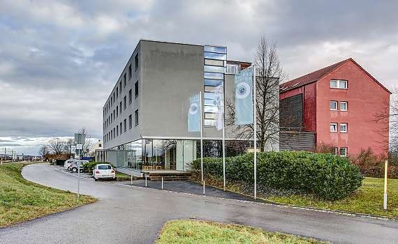 Modernes Hotel mit grauer Fassade, großen Fenstern und Fahnen. Vor dem Gebäude sind Grünflächen und ein Parkplatz zu sehen., © Centro Hotels Modernes Hotel mit grauer Fassade, großen Fenstern und Fahnen. Vor dem Gebäude sind Grünflächen und ein Parkplatz zu sehen., © Centro Hotels