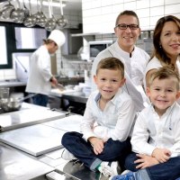 Familie in einer Restaurantküche, zwei Kinder sitzen auf einem Tisch, Eltern dahinter, Koch im Hintergrund., © Restaurant & Hotel Traube Hanweiler