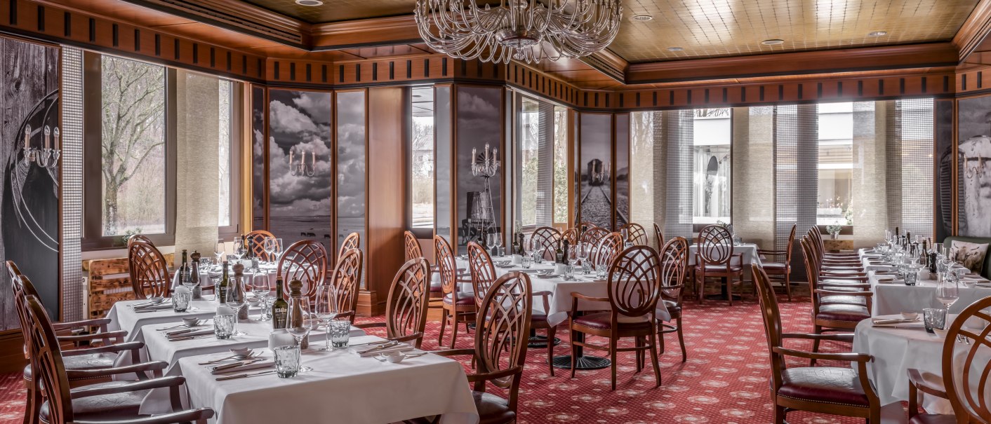 Elegantes Steakhouse mit weißen Tischdecken, Holzstühlen und Kronleuchter. Roter Teppichboden und große Fenster sorgen für eine warme Atmosphäre., © copyright by Kilian Blees