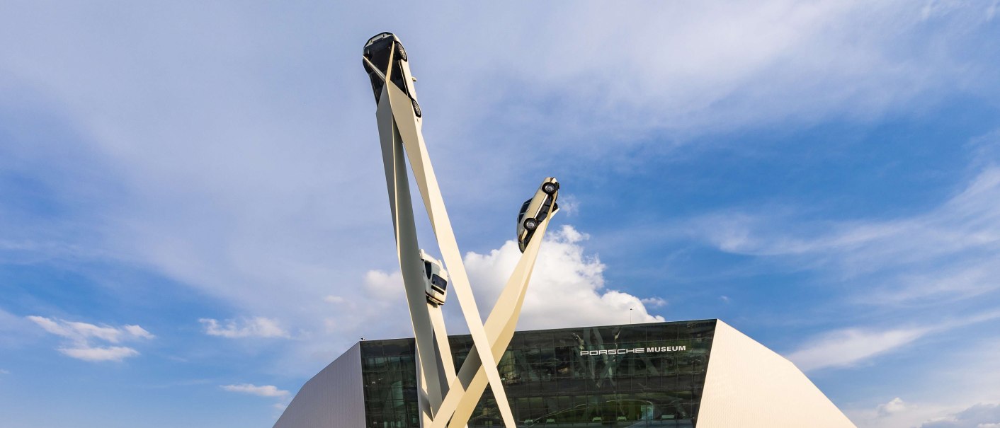 Das Porsche Museum mit moderner Architektur und einer Skulptur von drei Autos auf hohen Säulen vor blauem Himmel., © Stuttgart-Marketing GmbH, Werner Dieterich