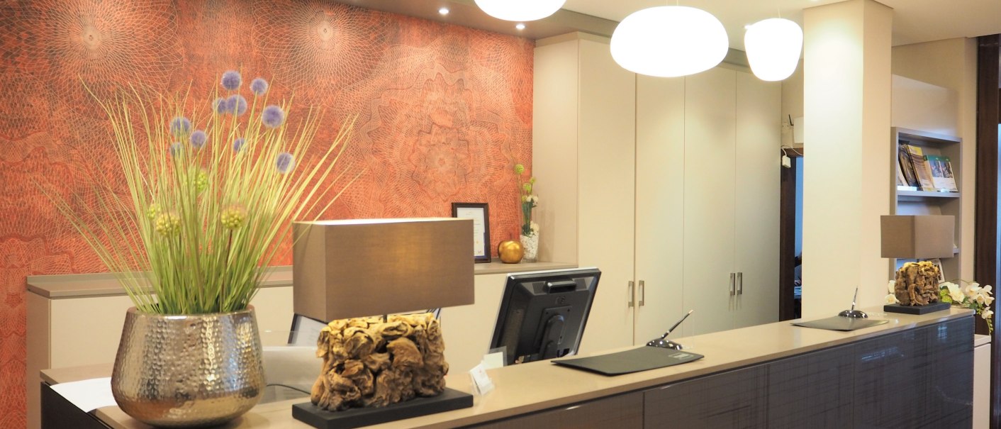 Moderne Rezeption mit stilvoller Dekoration, Pflanzen und Beleuchtung. Die Wand hat ein kunstvolles Muster, und es gibt einen Computer auf dem Tresen., © Hotel Fuchsen Moderne Rezeption mit stilvoller Dekoration, Pflanzen und Beleuchtung. Die Wand hat ein kunstvolles Muster, und es gibt einen Computer auf dem Tresen., © Hotel Fuchsen