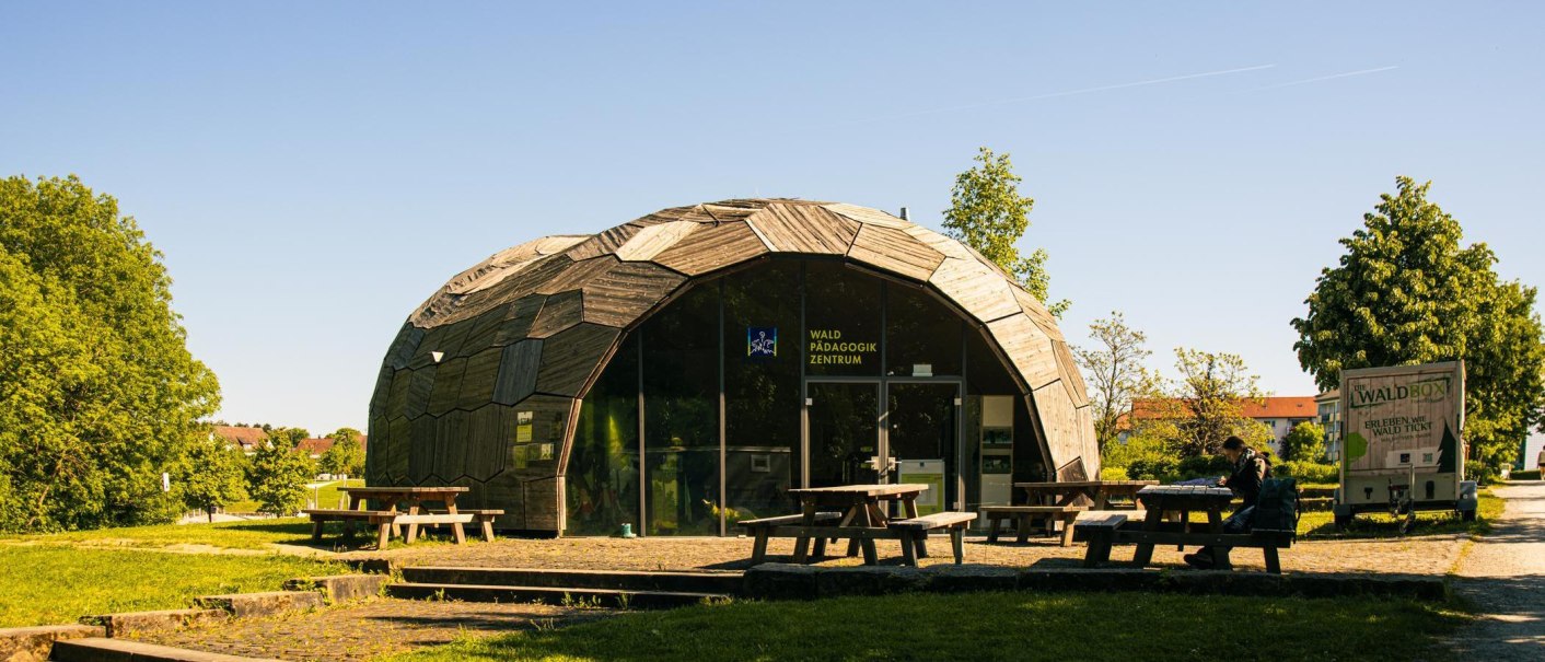 Ein modernes, kuppelf&ouml;rmiges Geb&auml;ude mit Holzverkleidung und Glasfront, umgeben von B&auml;umen und Picknicktischen im Freien., &copy; Stuttgart-Marketing GmbH, Sarah Schmid