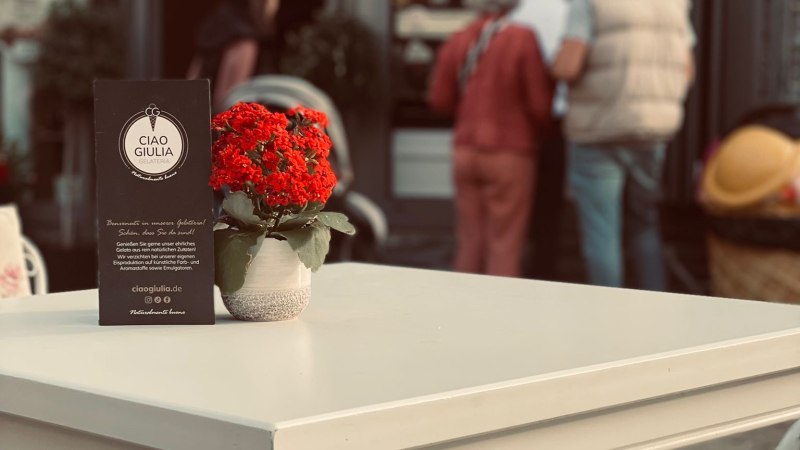 Ein wei&szlig;er Tisch mit roter Blume steht vor der Eisdiele 'Ciao Giulia'. Im Hintergrund sind Menschen zu sehen., &copy; Ciao Giulia
