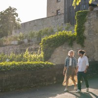 Ein Paar spaziert an einer alten Steinmauer entlang, umgeben von gr&uuml;nen Pflanzen und Weinreben, bei sonnigem Wetter., &copy; Stuttgart-Marketing GmbH, Martina Denker