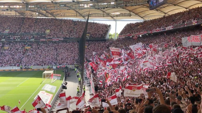 Blick in die Cannstatter Kurve der Mercedes-Benz Arena Stuttgart. Fans schwenken rot-weiße Fahnen und halten Banner hoch. Die Tribünen sind voll besetzt., © Stuttgart-Marketing GmbH