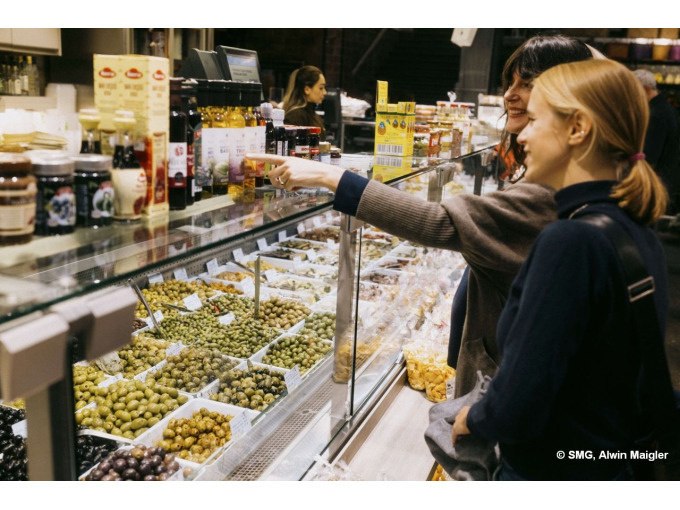 Zwei Frauen stehen an einem Marktstand mit Oliven und &Ouml;len. Sie zeigen auf Produkte hinter einer Glasvitrine. Im Hintergrund ist eine Verk&auml;uferin zu sehen., &copy; Stuttgart Marketing GmbH