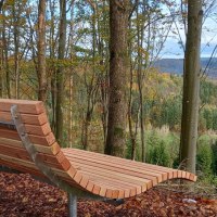 Holzbank am Aussichtspunkt im Wald, umgeben von Bäumen. Im Hintergrund eine weite, grüne Landschaft unter bewölktem Himmel., © Stadt Gaildorf