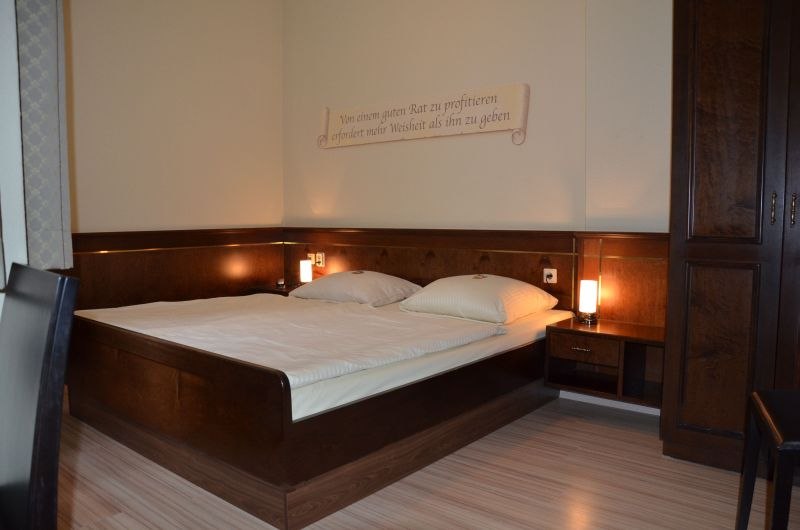 Gemütliches Doppelzimmer mit großem Bett, zwei Nachttischen und Wanddekoration. Holzmöbel und warme Beleuchtung schaffen eine einladende Atmosphäre., © TOMAS