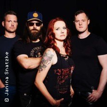 Vier Personen stehen in dunkler Kleidung vor einem schwarzen Hintergrund. Eine Frau mit roten Haaren steht vorne., © links im Bild