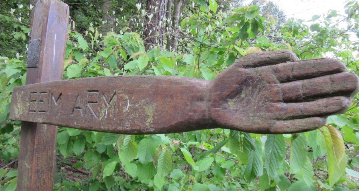 Holzskulptur eines ausgestreckten Arms mit der Inschrift 'BEIM ARM' vor grünem Laub im Wald., © Natur.Nah. Schönbuch & Heckengäu Holzskulptur eines ausgestreckten Arms mit der Inschrift 'BEIM ARM' vor grünem Laub im Wald., © Natur.Nah. Schönbuch & Heckengäu