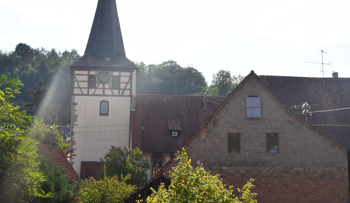Kirchturm der Johanneskirche mit Fachwerk, umgeben von Bäumen und alten Gebäuden. Der Himmel ist klar und sonnig., © Land der 1000 Hügel - Kraichgau-Stromberg Kirchturm der Johanneskirche mit Fachwerk, umgeben von Bäumen und alten Gebäuden. Der Himmel ist klar und sonnig., © Land der 1000 Hügel - Kraichgau-Stromberg