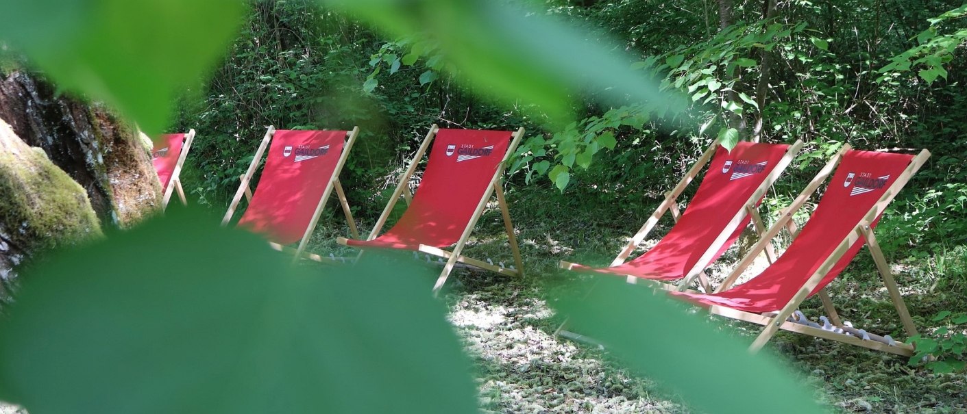 Fünf rote Liegestühle inmitten von Büschen, durch Blätter betrachtet, © Stadt Gaildorf