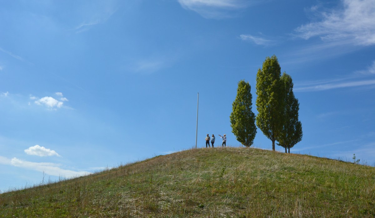 Drei Personen stehen auf einem grasbewachsenen Hügel neben zwei Bäumen und einem Fahnenmast unter klarem, blauem Himmel., © Remstal Tourismus e.V. Drei Personen stehen auf einem grasbewachsenen Hügel neben zwei Bäumen und einem Fahnenmast unter klarem, blauem Himmel., © Remstal Tourismus e.V.