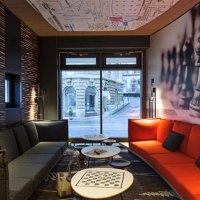 Moderner Raum mit grauen und roten Sofas, Schachbrettmuster auf Tisch, Wand mit Schachfiguren, Fenster mit Blick auf Geb&auml;ude., &copy; TOMAS